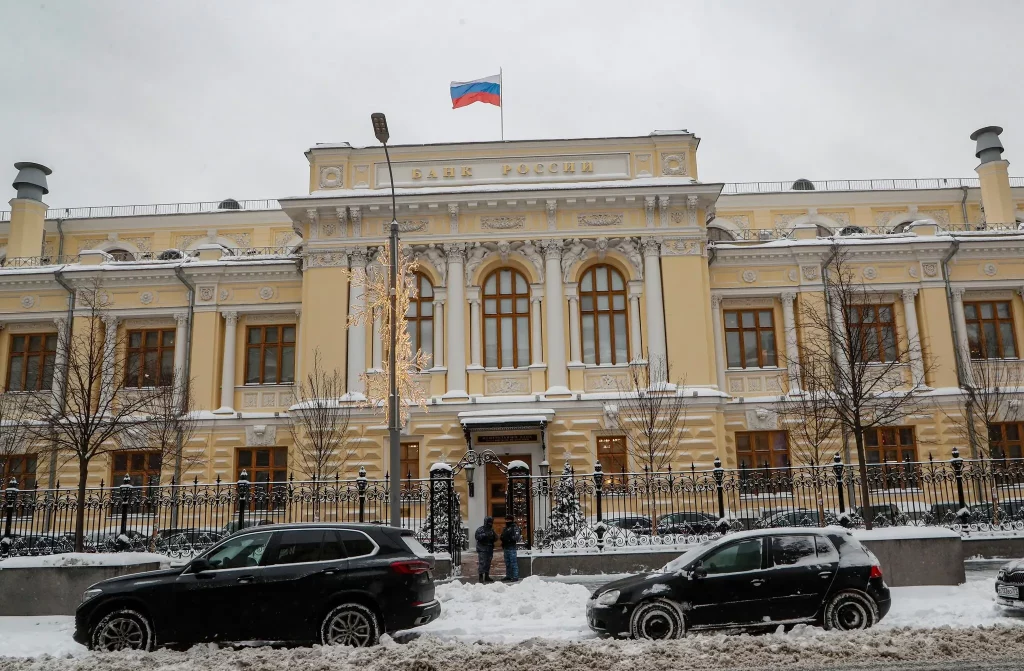 دفتر بانک مرکزی روسیه در مسکو، ساختمانی به رنگ کرم روشن در خیابانی پوشیده از برف، با پرچم روسیه در بالای ورودی.
